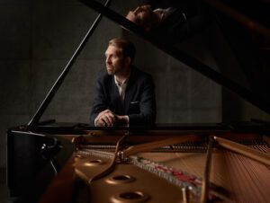 Lief Ove Andsnes sits at a grand piano and looks to his right ponderously.