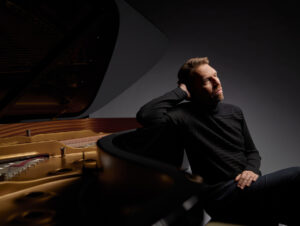 Lief Ove Andsnes sits with his back and arm propped up against a grand piano.