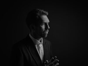 Black and white photo of Lief Ove Andsnes wearing a suit with his hands clasped in front of him.
