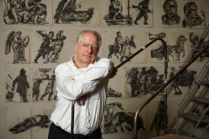 Willam Kentridge leans on a small ladder in front of his wall of sketches.