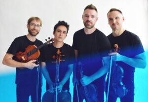 The four men of the JACK Quartet wearing matching plain black t-shirts as they hold their instruments, a blue filter coloring the bottom half of the image.