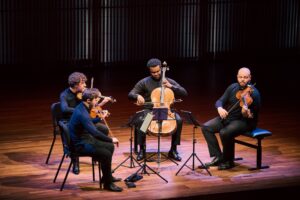 The four men of the Isidore Quartet perform their instruments on a dimly lit stage.