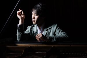 Bruce Liu, a young Chinese-Canadian man, sits at a piano looking to his right in a contemplative pose.