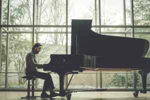 Daniil Trifonov, a young Russian man in a beige sweater, plays the grand piano in front of a wall of windows.