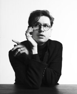 A black-and-white image of Vikingur Olafsson, an Icelandic man wearing tortoise shell glasses, poses with his face in one hand, looking off to his right contemplatively.