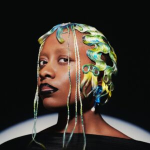 Cécile McLorin Salvant, a young Black woman with a blue and green hairdo of waves and braids, stares into the camera.