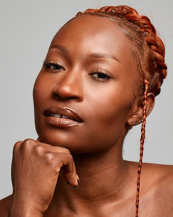 A portrait photo of Coral Dolphin from the Alvin Ailey American Dance Theater, a young black woman with a nose ring and red hair woven into an intricate braid on the crown of her head.