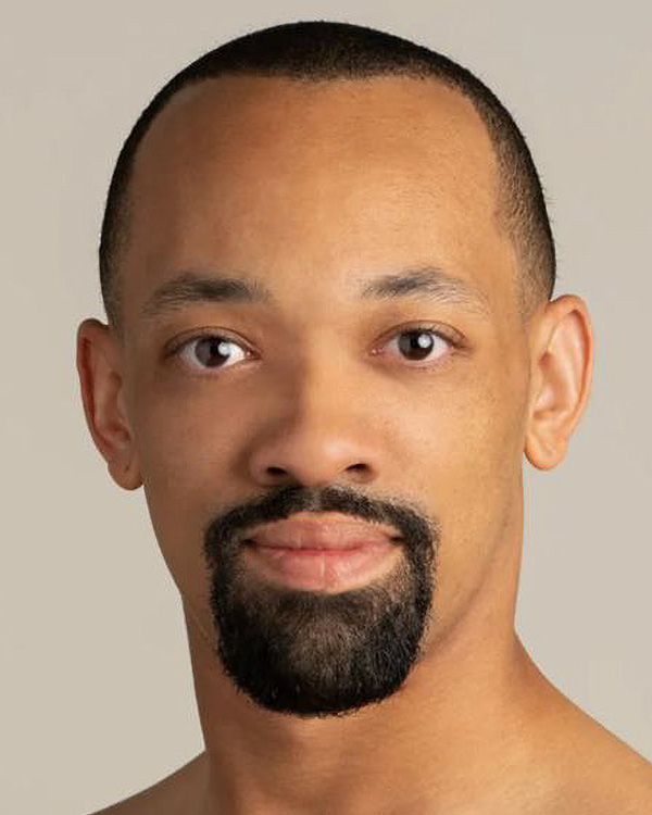 A portrait photo of Deanthony Vaughan from the Alvin Ailey American Dance Theater, a young black man with a shaved head and a neat goatee.