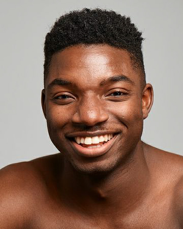 A portrait photo of Isaiah Day smiling brightly, a young black man with short dark hair, from the Alvin Ailey American Dance Theater.