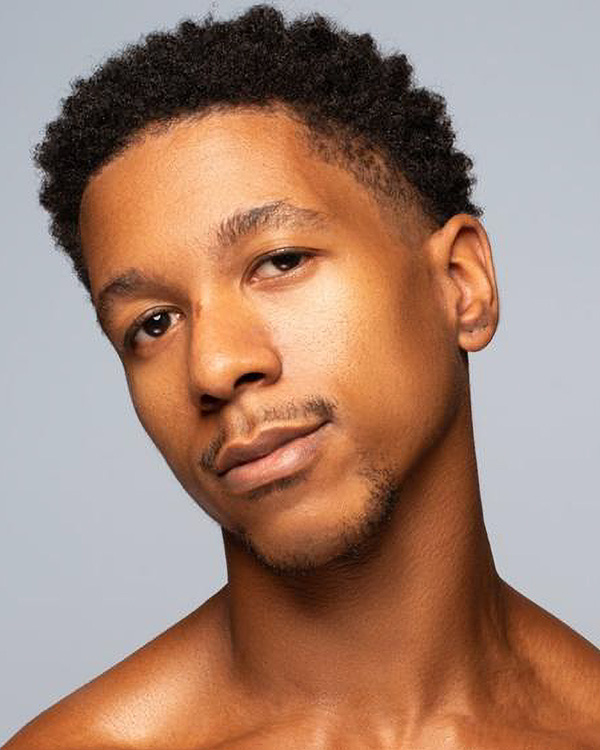 A portrait photo of Shawn Cusseaux from the Alvin Ailey American Dance Theater, a young black man with short curly hair and a light goatee.