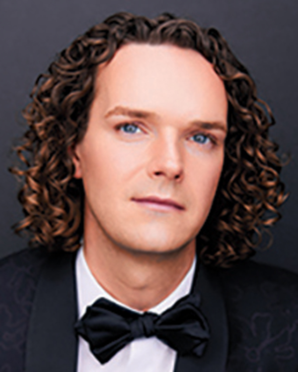A close up image of artist Brian Giebler, with brown curly hair wearing a suit and bow tie.