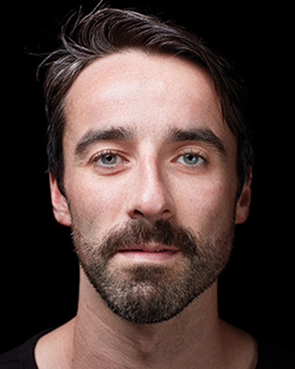 Close up portrait image of artist Brian Lawson, a young man with short brown hair and a close-shave beard.