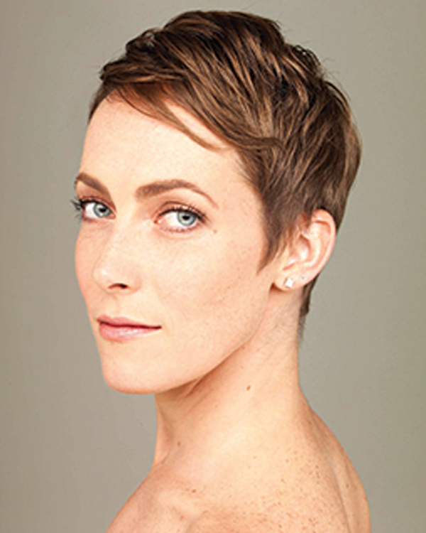 A portrait of artist Elisa Clark, looking over her shoulder with a short blonde pixie cut and diamond stud earrings.