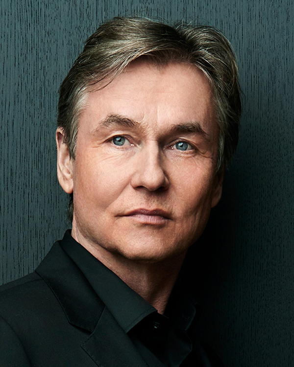Portrait of Artist Esa Pekka Salonen, a middle-aged white man with blonde hair, wearing a black suit and dress shirt.
