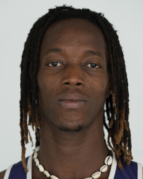 A close up photo of artist Inas Dasylva, a young black man with thin dreads and a puka shell necklace.