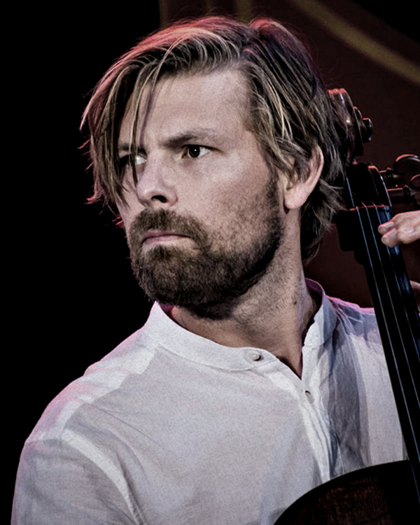 Artist Johannes Rostamo looks off camera with a serious expression in a close-up image of him playing his cello.