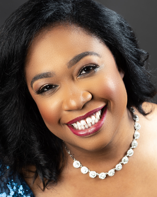 Michelle Cann wears a large diamond necklace and smiles brightly in this close up photo.