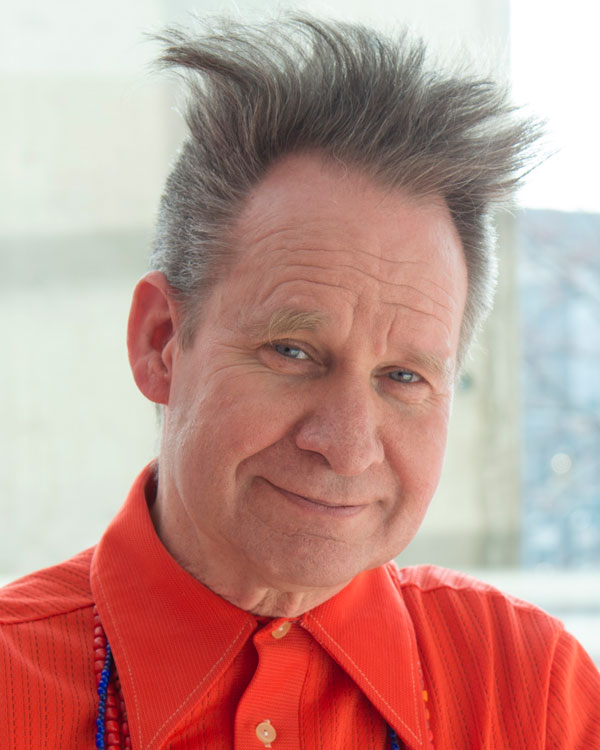 Artist Peter Sellars wears a bright red shirt and his hair in a style that sticks straight upwards.