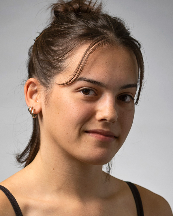 Adi Blumenreich, a light-skinned woman with medium length brown hair half pulled into a bun, slightly smiles towards the camera