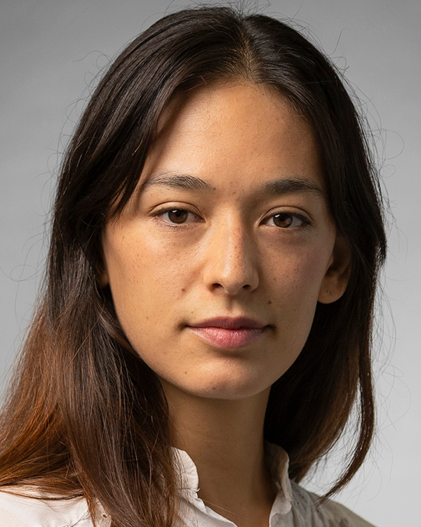 Adrienne Lipson, an olive-skinned woman with long brown hair and freckles, smiles slightly into the camera