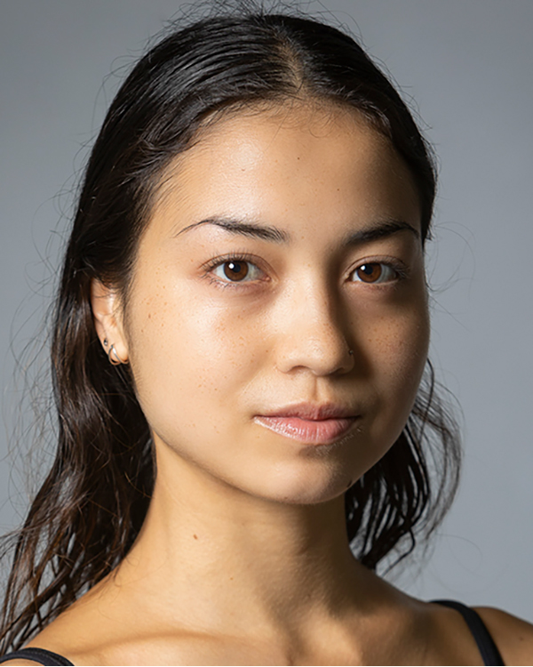 Annika Verplancke, a woman with olive skin and long, dark, wavy hair, smiles slightly into the camera