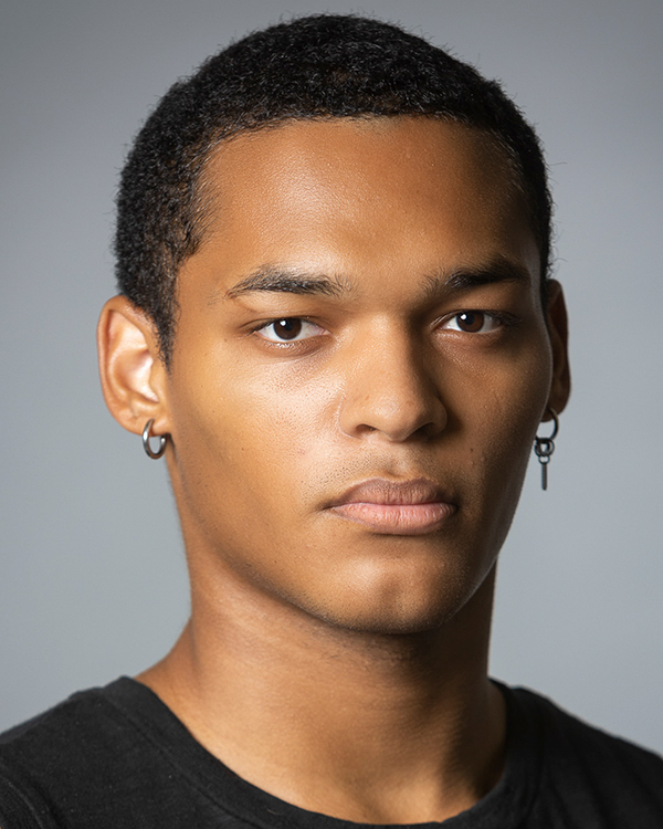 Bo Matthews, a black masculine-presenting person with short dark hair, looks into the camera