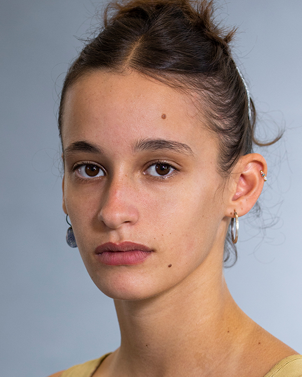 Danai Porat, a light-skinned woman with her brown hair pulled up, stares into the camera