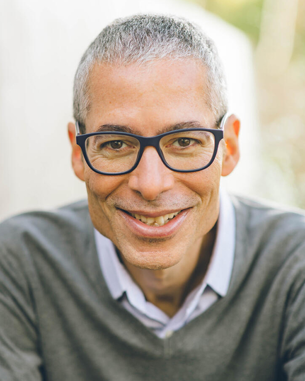 Dylan Penningroth, a man with short salt-and-pepper hair wearing boxy black glasses and a gray sweater, looks into the camera