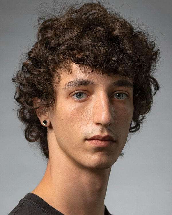 Emil Brukman, a man with olive skin, curly brown hair, and green eyes, looks into the camera