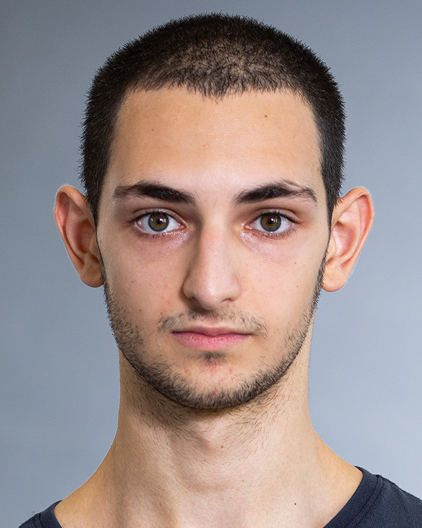 Guy Davidson, a light-skinned man with dark buzzed hair and hazel-green eyes, stares straight into the camera