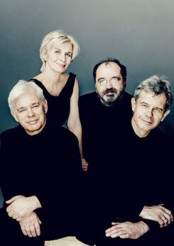 The four members of the Hagen Quartet, one woman and three men wearing all black, posed sitting close together