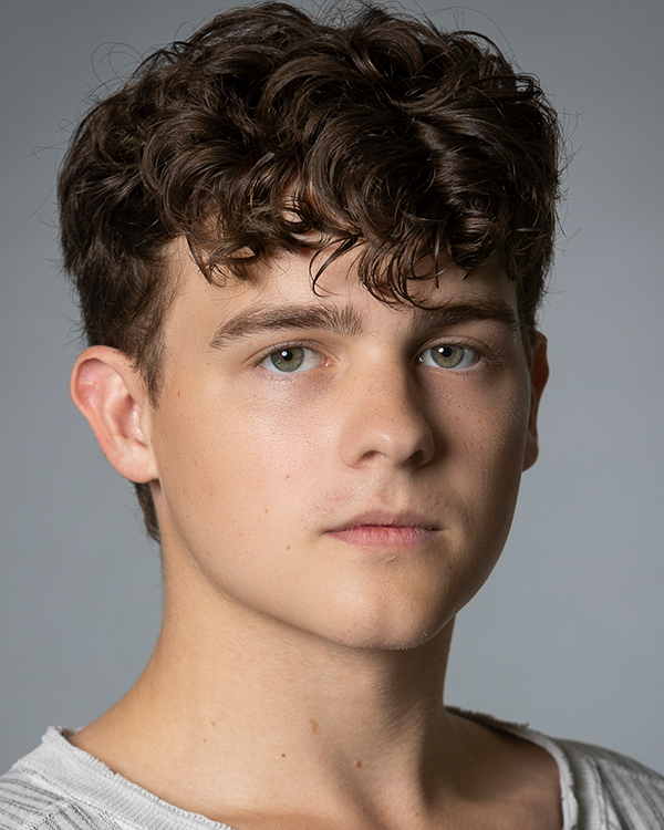 Holden Cole, a light-skinned man with curly brown hair and green eyes, looks into the camera