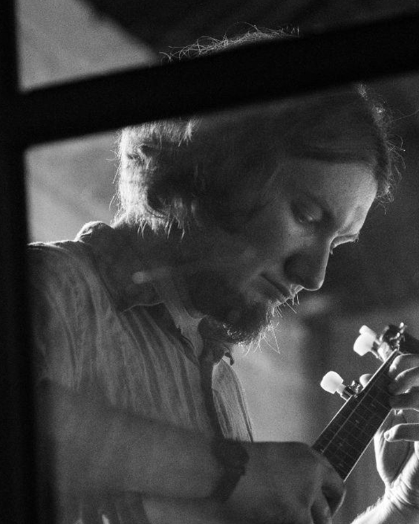 A black-and-white image of Janus Fouche, a young man with wispy hair, playing the banjo