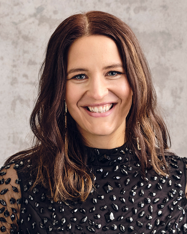 Lise Davidsen, a white woman with long brown hair, wearing a black-bedazzled dress smiles while looking at the camera.