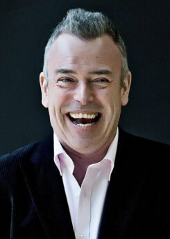 Malcolm Martineau, a white man with short salt and pepper hair, wearing a dark suit smiling widely while looking into the camera.