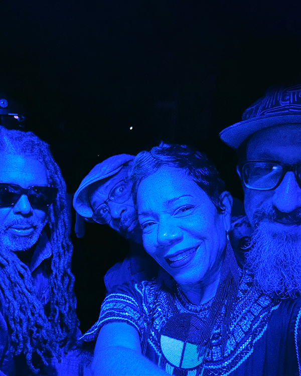 Three men and one woman taking a selfie onstage under strong blue lighting