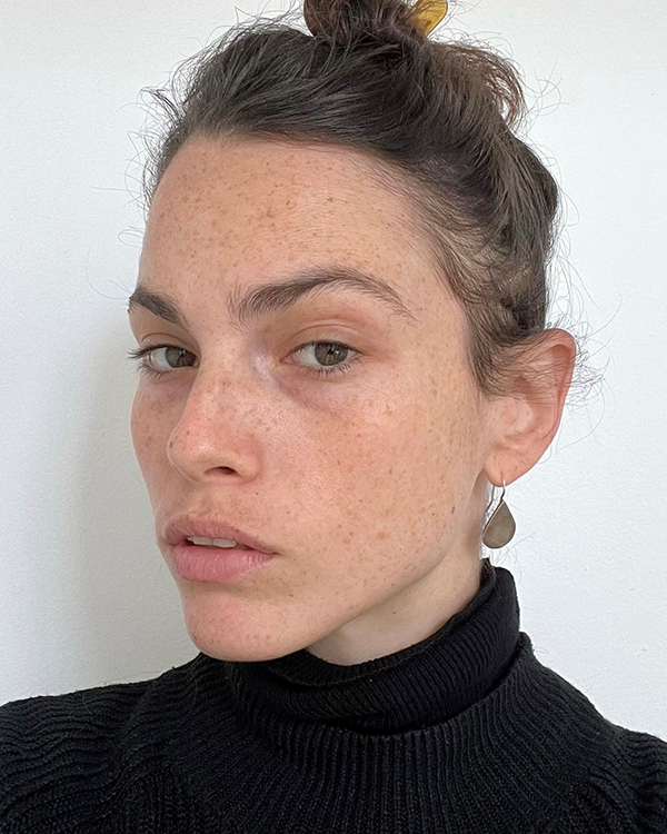 Ori Kroll, a light-skinned woman with freckles and her brown hair pulled up into a bun, looks into the camera