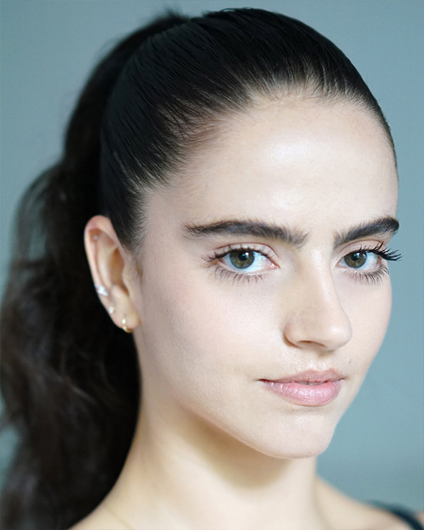 Daisy Jacobson, a fair-skinned woman with her long wavy hair pulled back in a ponytail, looks into the camera.