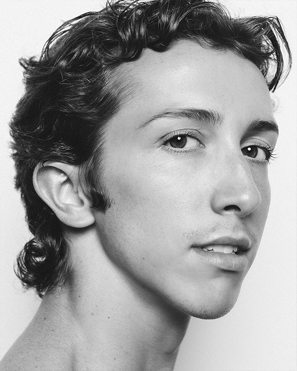 A black-and-white headshot image of Kyle Halford, a light-skinned man with medium-length curly hair, looking into the camera.