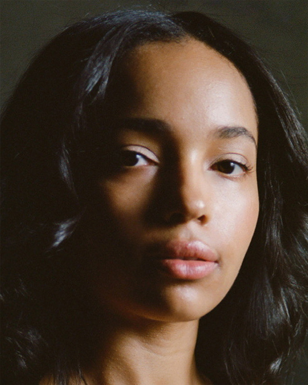 A headshot image of Miriam Gittens, a woman with medium-dark olive skin and long curled black hair looking into the camera.