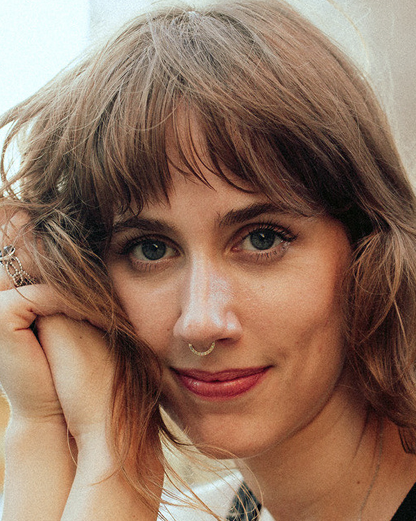 Molly Rumble, a white woman with short brown hair and bangs, looks into the camera, resting her head on her hands.