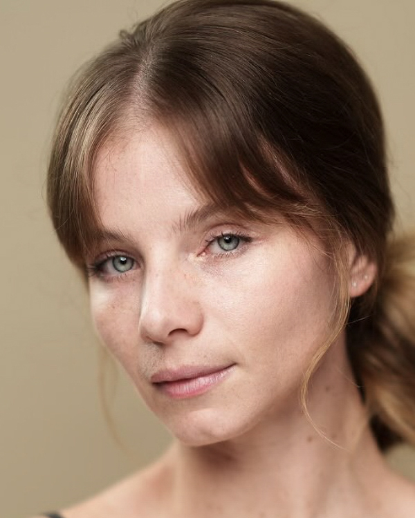 A headshot image of Nicole Ashley Morris, a white woman with light eyes and light brown hair tied back, looking into the camera.