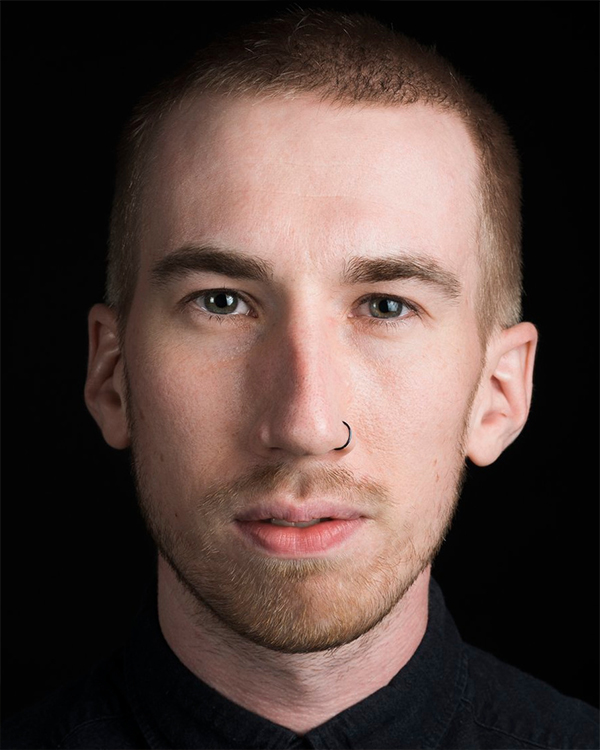 A headshot image of Oliver Greene-Cramer, a white man with a buzz cut, looking straight into the camera.