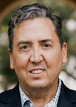 John Churchwell, an older white man with salt and pepper hair, smiles into the camera.