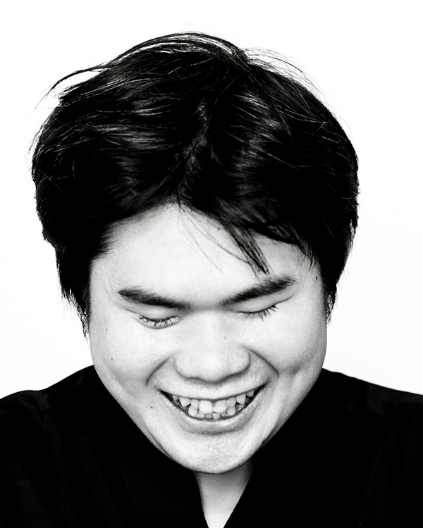 A black-and-white image of Nobuyuki Tsujii, a Japanese man, smiling widely with his eyes closed and head down.