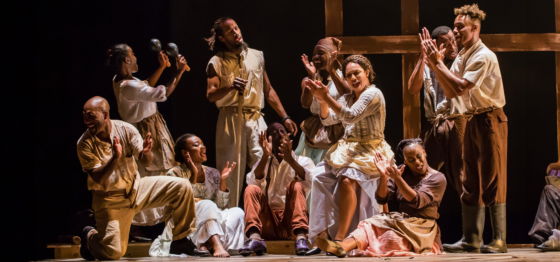 The Step Afrika! group of African American performers stand together on stage, expressively singing and clapping in unison.