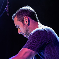 Antonio Sanchez plays the drums on a hazy stage with pink-toned lights amidst his performance of Birdman Live.