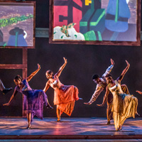 The Step Afrika! group of African American dancers perform on stage wearing bright clothing, with large colorful screens in the background.