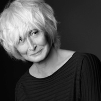 Close up image of Twyla Tharp smiling softly, with short white hair in a black long sleeve top.