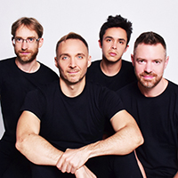 The four men of the JACK Quartet wearing matching plain black t-shirts in front of a plain white background.